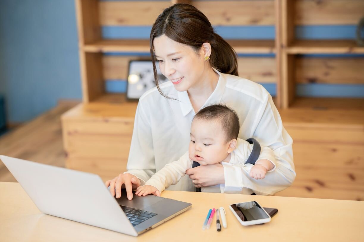 赤ちゃんを抱えてノートパソコンを操作する女性